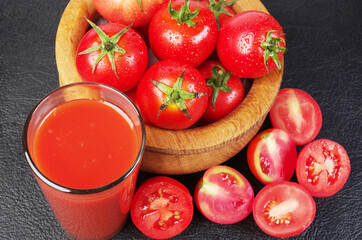 A glass of tomato juice and red tomatoes on a black table.