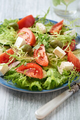 Salad with Green Olives, Tomatoes and Feta Cheese. Bright wooden background. Close up. 