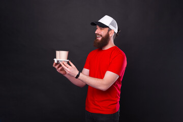 Photo of joyful man with beard giving someone two coffee cups to go over black background