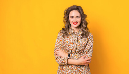 Portrait of young lady in dress standing over yellow background with crossed arms and looking at the camera