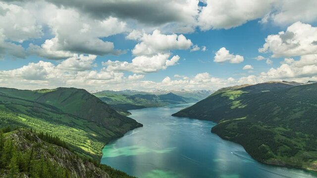 Timelapse of fluffy white clouds flowing over huge lake in middle of green mountains on a bright summer blue sky day