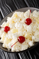Glorified Rice is a cold dessert salad made with rice, crushed pineapple, marshmallows, sweetened whipped cream, and maraschino cherries close-up in a plate on the table. Vertical