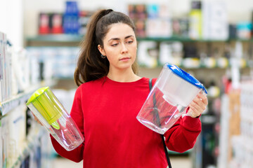 Portrait of young woman chooses between two carafe with a water filter in a home appliance store....