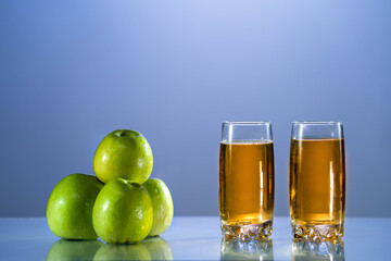 Two glasses of apple juice with green apples in theblue background. yellow background. Reflected surface. Summer day. Good mood. Fresh juice