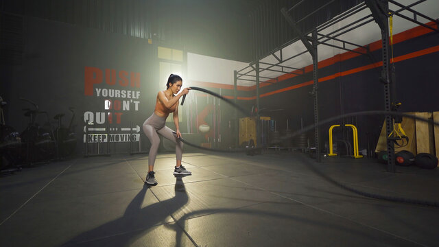 Asian woman doing battle ropes for cardio. Muscle strength training workout at gym fitness center club. Exercise indoor with sport equipment. Athletic. People lifestyle. Recreation