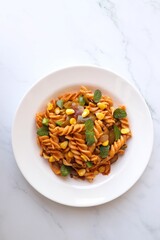 Whole wheat fusilli pasta with vegetables. Vegetable Pasta with zucchini, mushrooms, corn, and peppers on a white plate. Garnished with mint leaves. on a white marble table with cutlery. copy space.