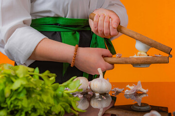 Female chef using a vintage garlic press along with fresh vegetables on black reflexive glass and...