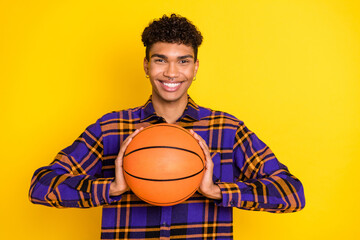 Photo portrait of young man keeping basket ball smiling in casual clothes isolated vivid yellow color background