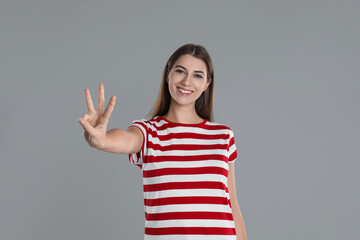 Woman showing number three with her hand on grey background