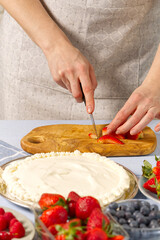woman baker cuts strawberries for strawberry cake. Homemade strawberries cake made from meringue cake and cream with strawberries. home cooking concept