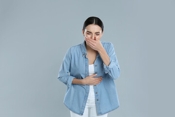 Woman suffering from stomach ache and nausea on grey background. Food poisoning