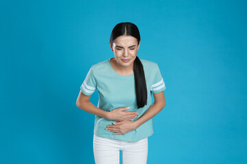 Woman suffering from stomach ache on light blue background. Food poisoning