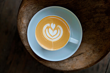 Top view shot of white cup with cappuccino hot beverage with foam, with plate on wood textured table. Latte art concept. Close up, copy space for text, wooden background.