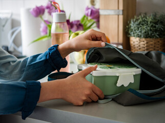 Schoolboy teenager preparing lunch box putting food container into schoolbag. 