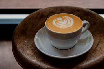 Top view shot of white cup with cappuccino hot beverage with foam, with plate on wood textured table. Latte art concept. Close up, copy space for text, wooden background.