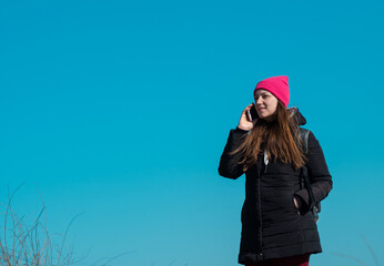 Young confident woman in pink hat with smartphone in hand calling friends walking on city background blue sky. Stylish millennial girl outdoor lifestyle authentic photo. Real people, solo travelling