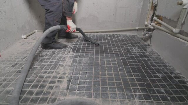 A man vacuums a construction site. Close-up of a cleaner in special clothing holding a brush from an industrial professional vacuum cleaner. A worker vacuums the bathroom floor before laying.