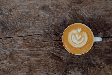 Top view shot of white cup with cappuccino hot beverage with foam, with plate on wood textured table. Latte art concept. Close up, copy space for text, wooden background.