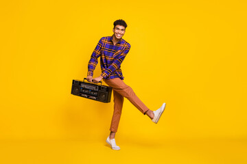 Full length portrait of funny carefree dark skin man dancing hands carry boombox isolated on yellow color background