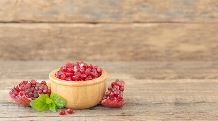Pomegranate seeds in a wooden bowl and slicces of pomegranate on a wooden background