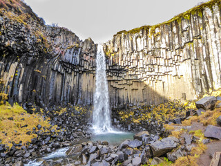 A majestic waterfall, surrounded by dark lava columns. Black columnar basalt formations beautifully frame the waterfall and give it its name, Black Fall. Romantic place in the nature, hidden gem.