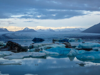 Beautiful glacier lagoon. Thousands of icebergs drifting lazily towards the sea, shining in many shades of blue. Soft sunset in the back. Thick clouds above the lagoon. Glacier's cap in the back