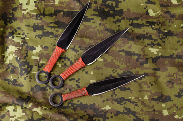 Fototapeta na wymiar Black Throwing knives on camouflage cloth.