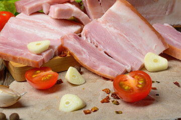 Smoked sliced pork belly, bacon, ham with herbs, tomatoes and black pepper on food paper. Wooden rustic background.Selective focus.