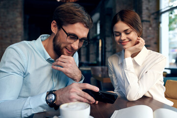 Cheerful man and woman are sitting in a cafe at the table working communication technology