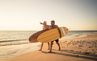 Two senior surfers with surfboard having fun on empty remote beach enjoying retirement lifestyle