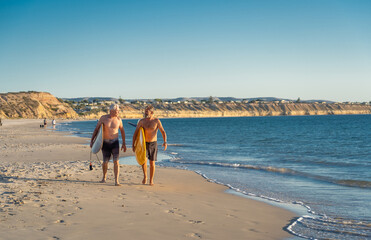 Two senior surfers with surfboard having fun on empty remote beach enjoying retirement lifestyle