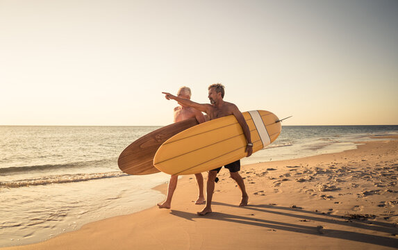 Two senior surfers with surfboard having fun on empty remote beach enjoying retirement lifestyle - Powered by Adobe