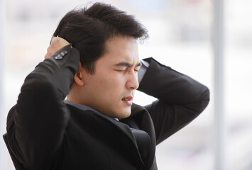 Closeup portrait shot of Asian young black short hair stress depress unhappy male businessman worker in formal suit hold hands up on head has trouble and problem in work at office blurred background