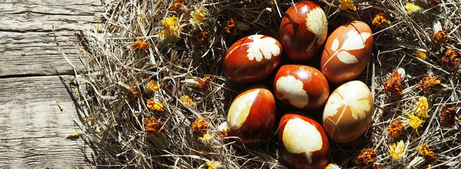 Painted Easter eggs in a nest of hay with dried marigold flowers on a wooden natural background.Easter background with place for text.