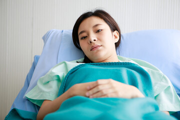 Asian young sick ill female patient wears green hospital uniform lay down on bed lean on blue...