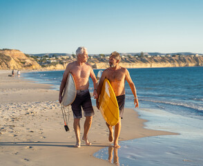 Two senior surfers with surfboard having fun on empty remote beach enjoying retirement lifestyle