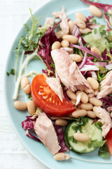 Tuna salad with tomatoes, cannelloni bean and endive. Bright wooden background. Top view. Close up. 