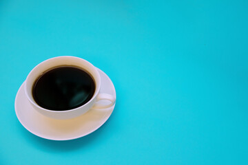 White cup with black coffee on a blue background. Morning breakfast.Empty space for the text.