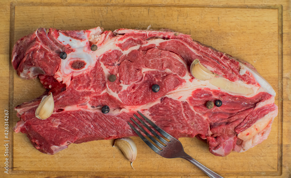 Wall mural on a fresh piece of beef is a fork, garlic and pepper. under it is an old cutting board