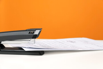 Stapler on white table against bright orange background. Minimalistic, vivid colors. Office supplies.