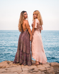 A couple of Caucasian girls in beautiful dresses enjoying the summer, holding hands in an affectionate way by the sea