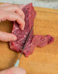 On a cutting board, red beef meat is cut with a knife