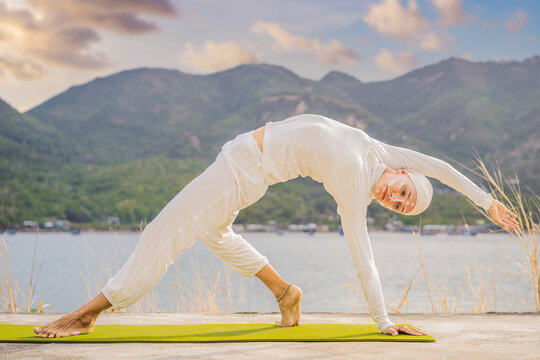 Kundalini yoga woman in white clothes and turban practices yoga kundalini on the background of the sea, mountains and sunset. Fighting face painting of the Indians shows her inner world. Visual