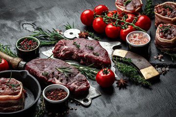 raw three beef steaks on over meat butcher knife with spices dark background. top view.