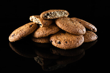 Oatmeal cookies with chocolate chips are isolated on a black background with a reflection. Lots of brown round homemade cookies lying on a reflective surface, close-up