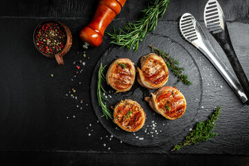 Medallions steaks from the beef tenderloin covered bacon on grill Dark background. Cooking beef steak on grill by chef hands