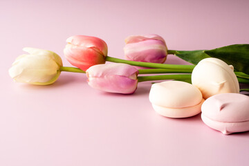 Obraz na płótnie Canvas Colorful tulips and sweets on a pink background. Festive bright spring background. A bouquet of flowers and marshmallows. Greetings for March 8, birthday, Easter or Valentine s Day