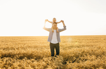 Happy family, young father with little son are walking in a wheat field at sunset in summer