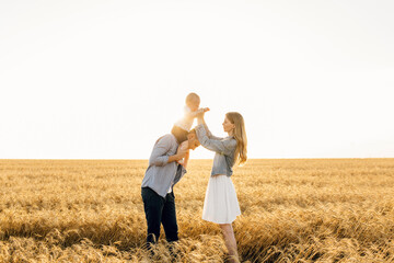 Fototapeta na wymiar Happy family, Mother, father and son walk in the wheat field and enjoy