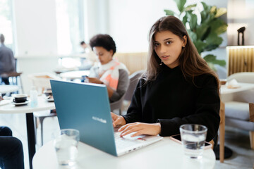 Fototapeta na wymiar Portrait of female student using net-book while sitting in cafe